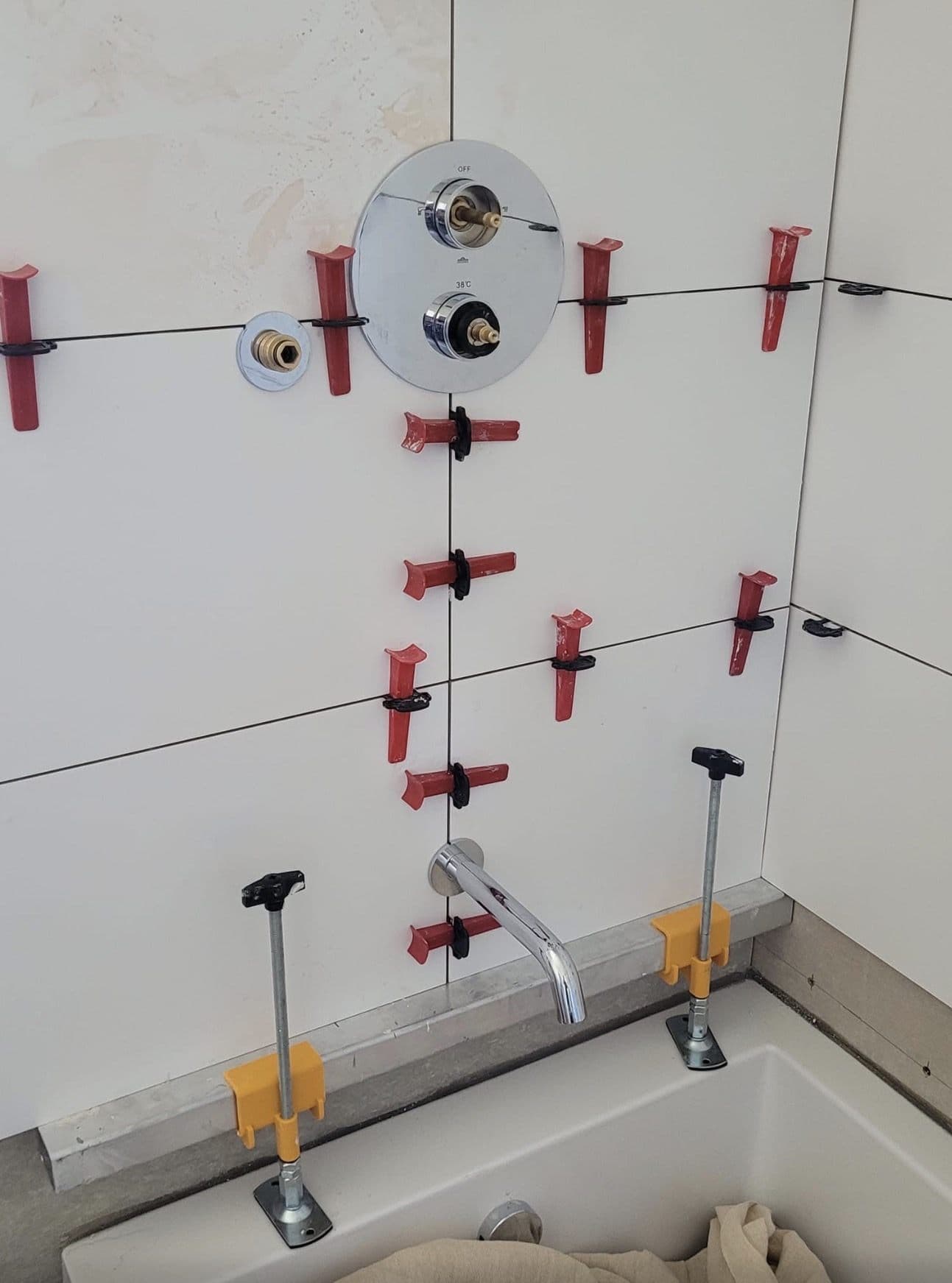 Tile levelling clips in place around a shower valve above a bath