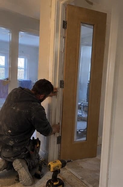 Wooden glazed internal door being hung in a new frame