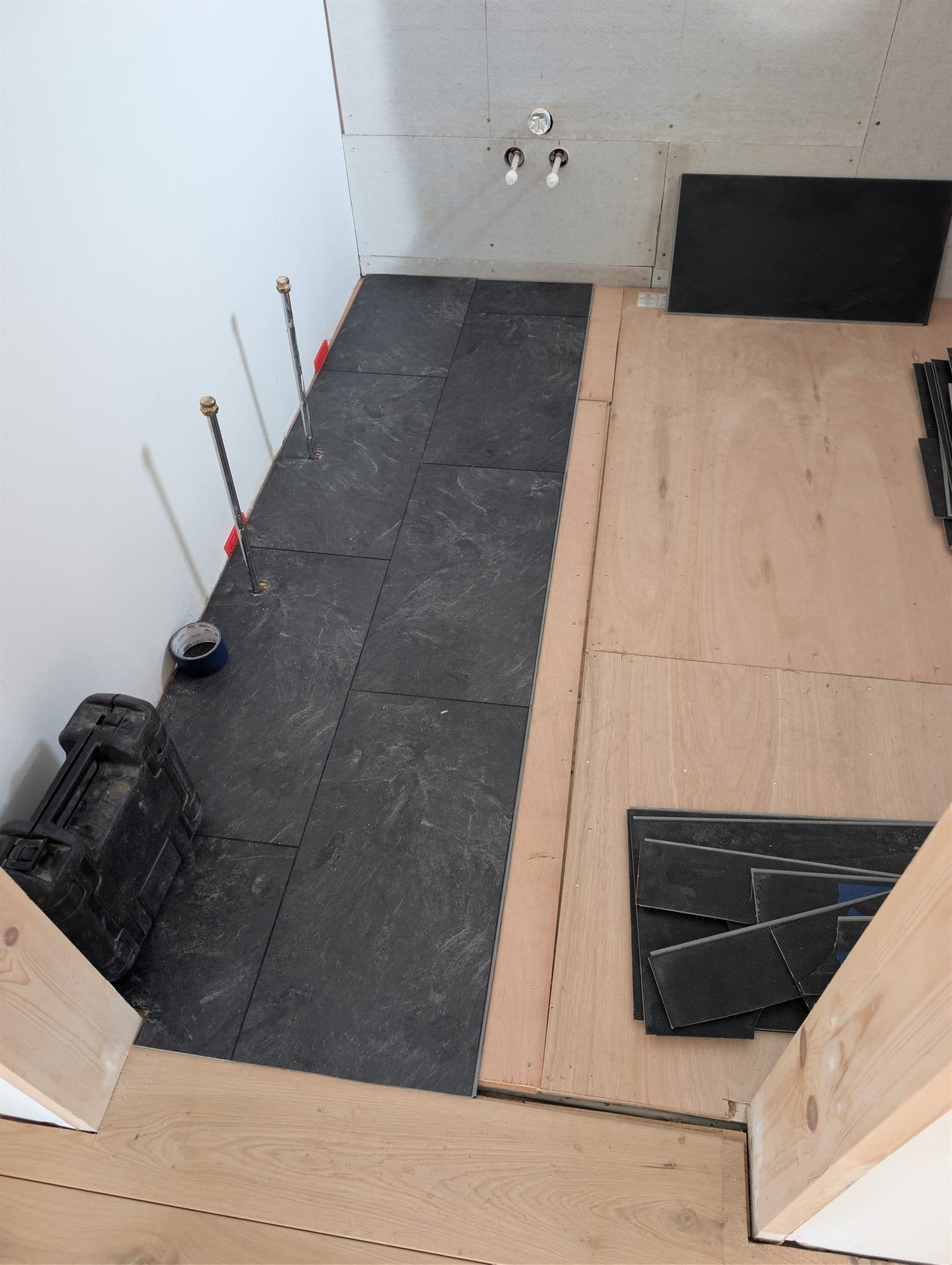 Dark floor tiles being laid over a prepared boarded subfloor