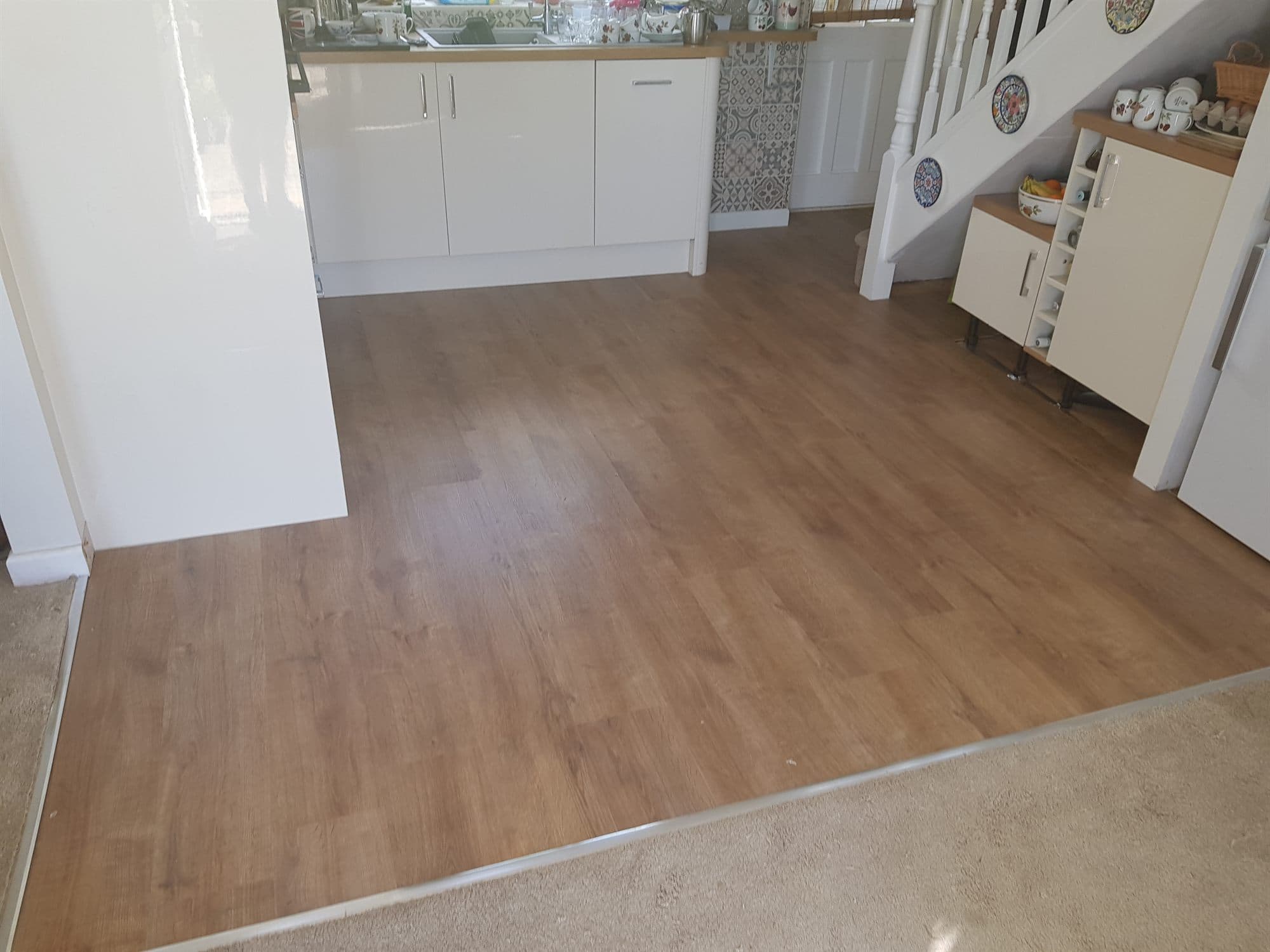 Kitchen and hallway finished with wood-effect flooring and a threshold trim to the carpet