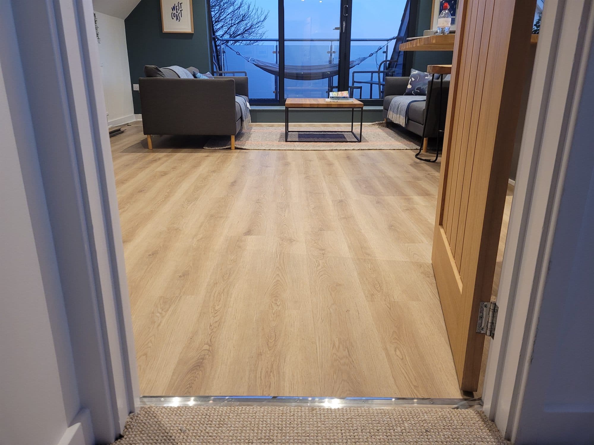 Oak-effect flooring running through a doorway into a lounge
