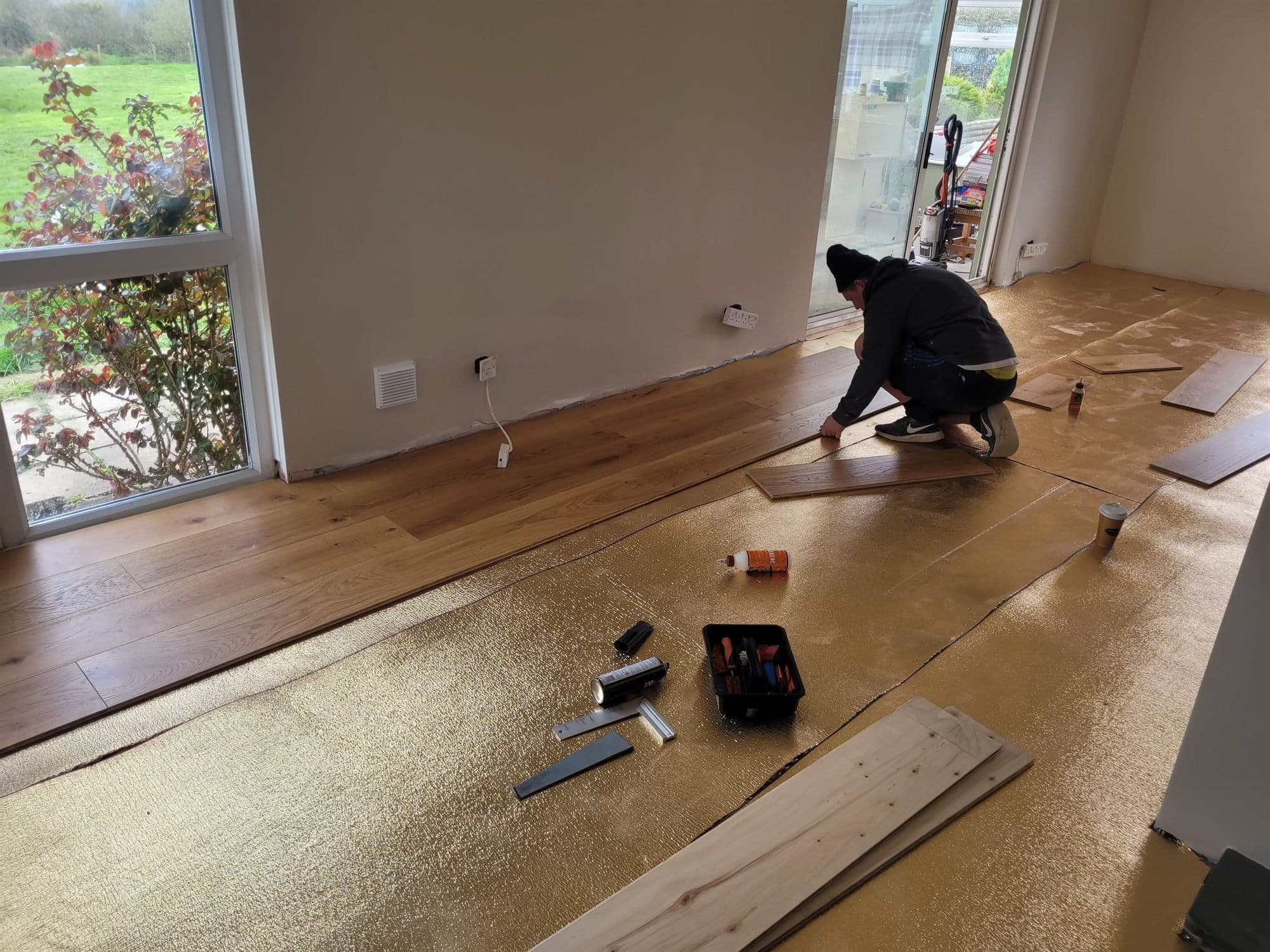 Wide wooden floorboards being laid over underlay in a large open-plan room
