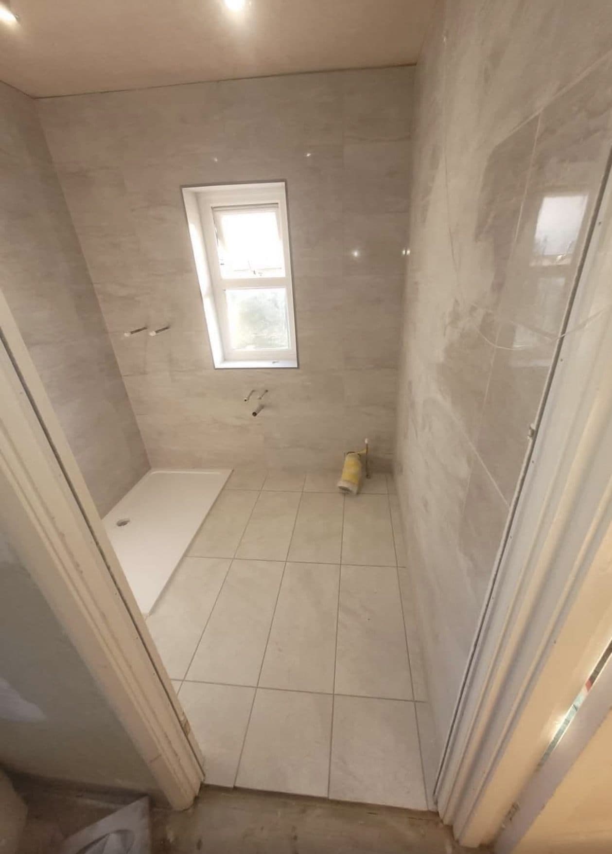 Small bathroom with walls and floor tiled and the bath in place, before fitting the suite