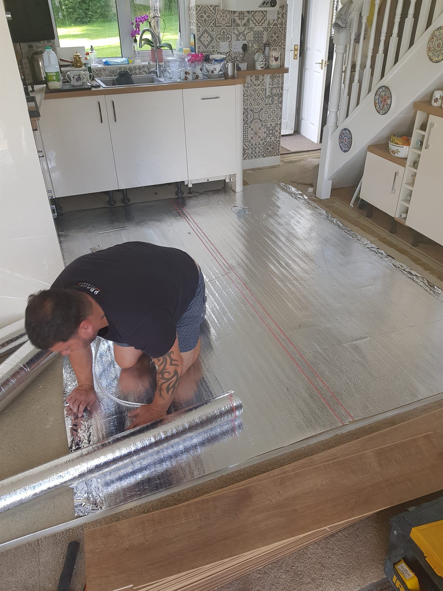 Foil-backed underlay being rolled out across a kitchen and hallway floor