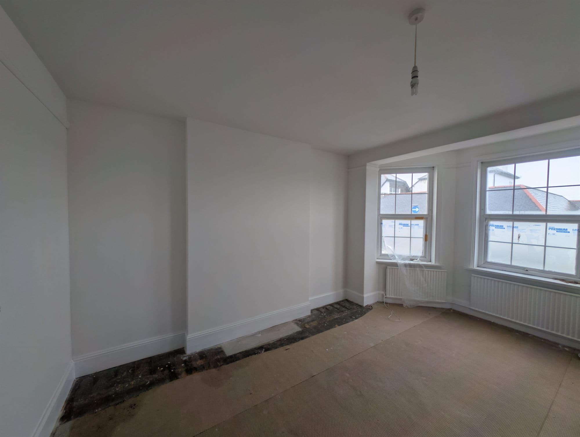 Front room with bay window after replastering and decorating, walls and woodwork finished in white