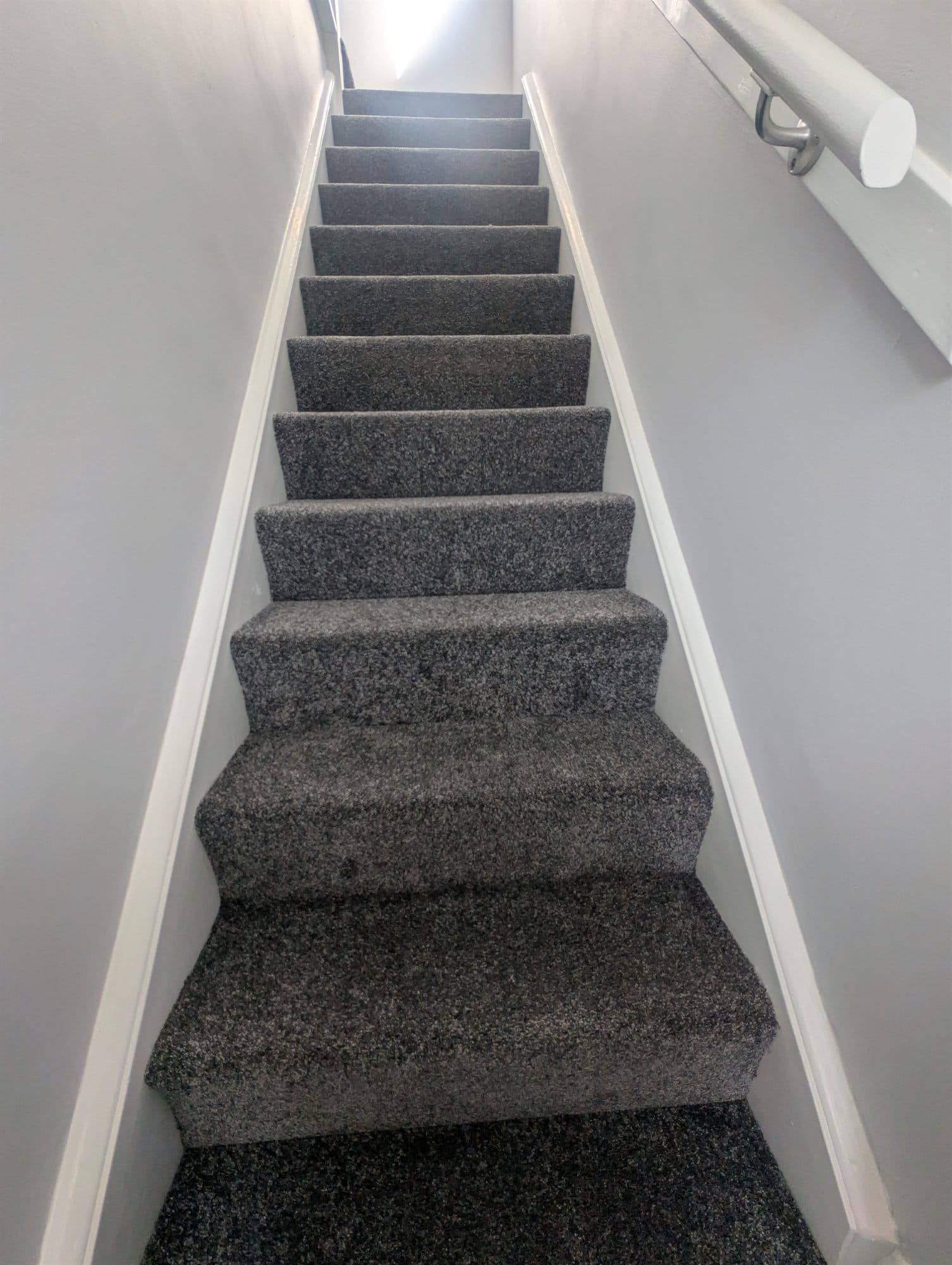 Narrow staircase finished with grey carpet, white skirting and freshly painted walls