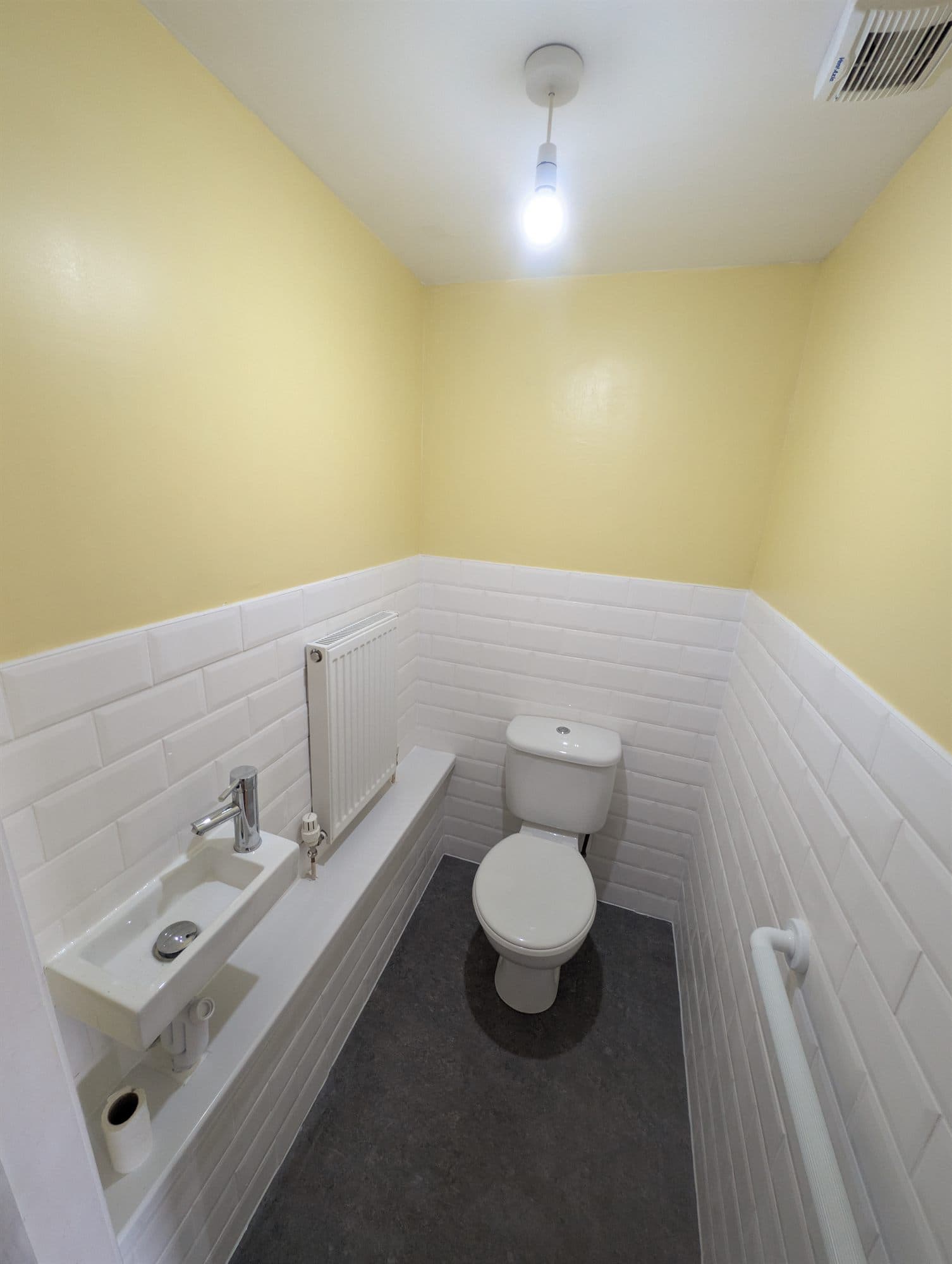 Finished downstairs WC with white metro wall tiles, pale yellow walls, compact basin and grey floor